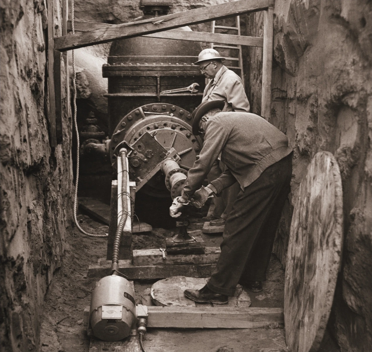 Historic photograph of Mr. Koppl and another worker operating hot tap equipment in a trench