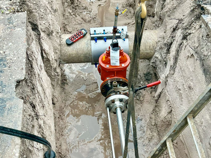 Hot tap machine and orange valve connected to a pipe in an excavation